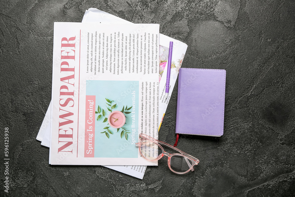 Newspapers with eyeglasses, notebook and pen on dark background