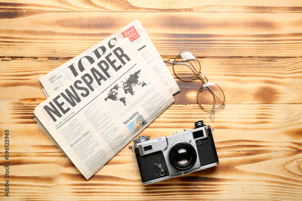 Newspapers with eyeglasses and photo camera on wooden background