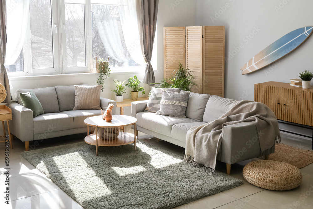 Interior of light living room with surfboard, houseplants and sofas