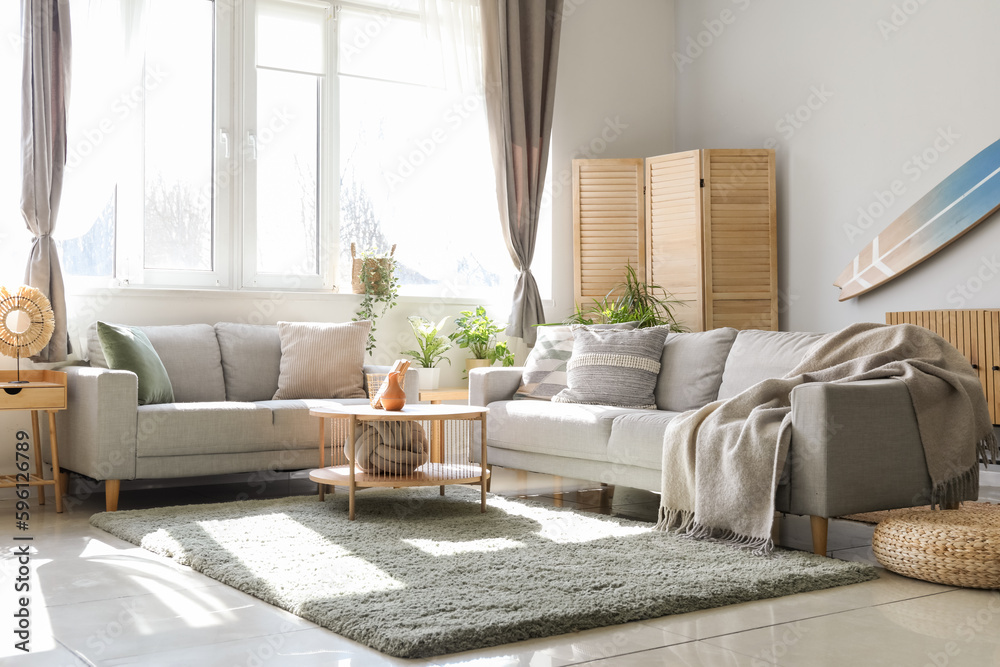 Interior of light living room with surfboard, houseplants and sofas