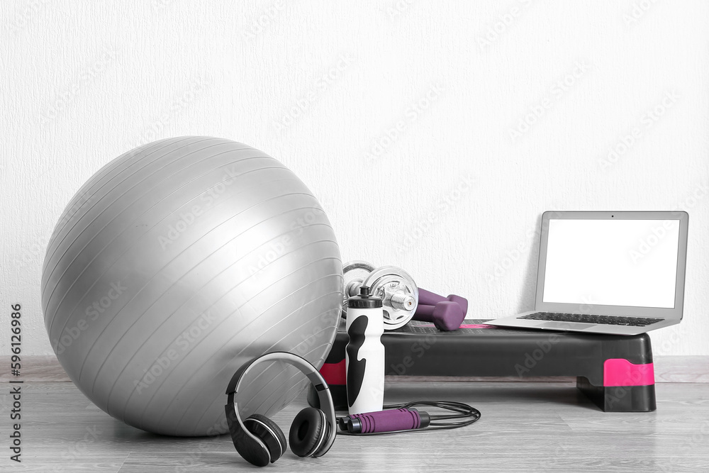 Laptop with sports equipment and headphones near white wall in gym