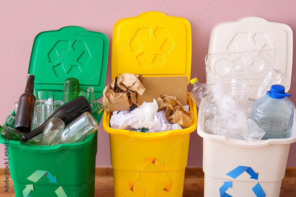 Trash bins with recycling symbol and different garbage near pink wall