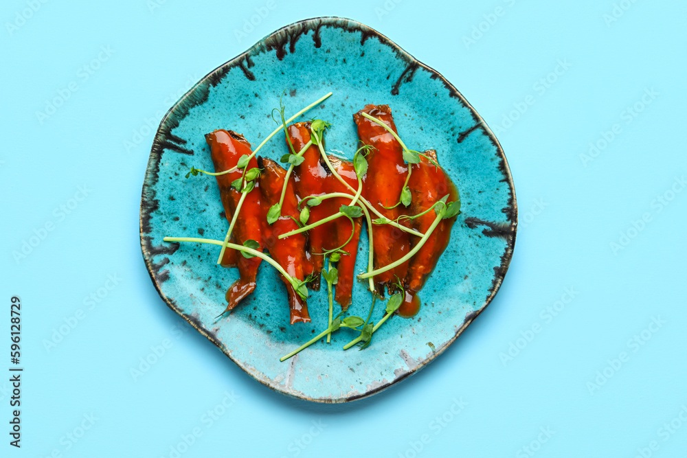 Plate with canned fish in tomato sauce and microgreens on blue background