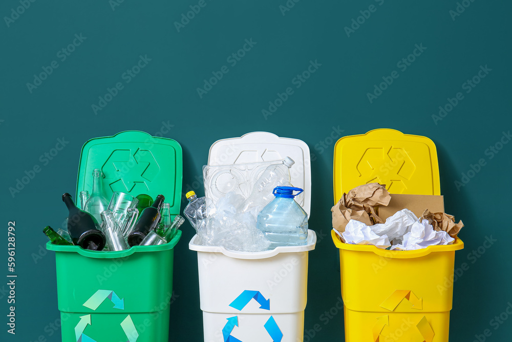 Trash bins with recycling symbol and different garbage near green wall