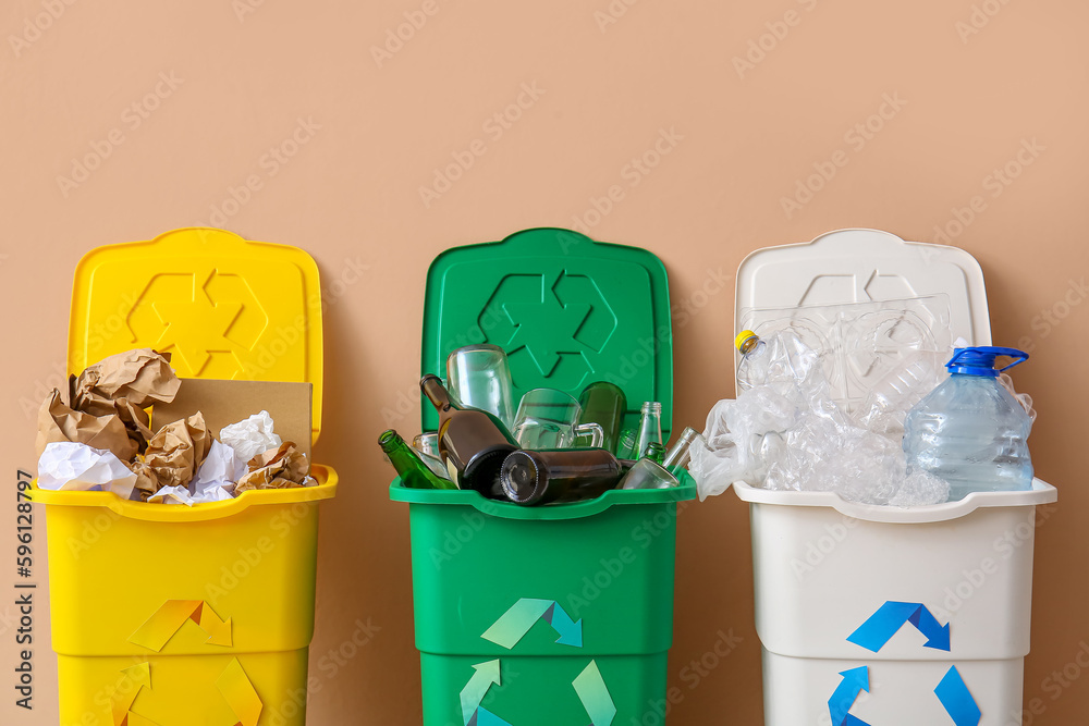 Trash bins with recycling symbol and different garbage near beige wall