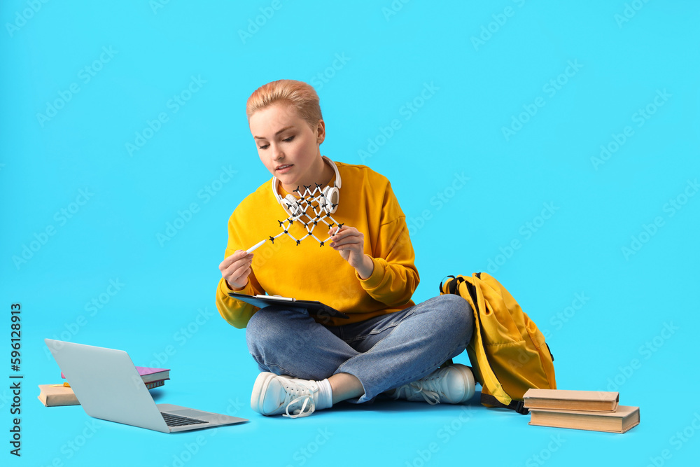 Female student studying with molecular model on blue background