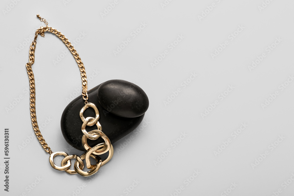 Black stones with golden necklace on light background