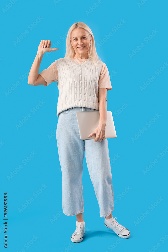 Mature female programmer with laptop pointing at herself on blue background