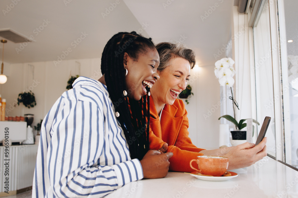 Two happy business women video calling their colleagues in a coffee shop