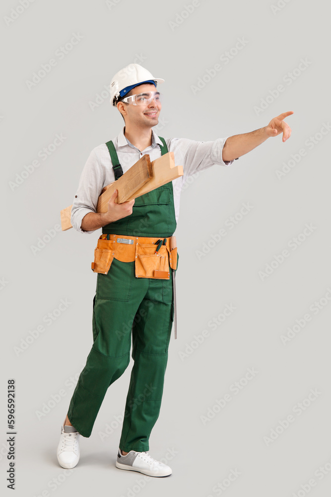 Young carpenter with wooden planks pointing at something on grey background