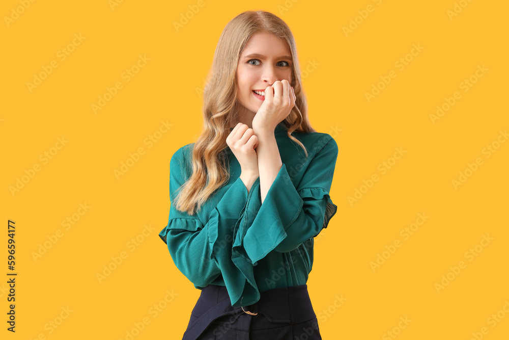 Happy young woman biting nails on yellow background