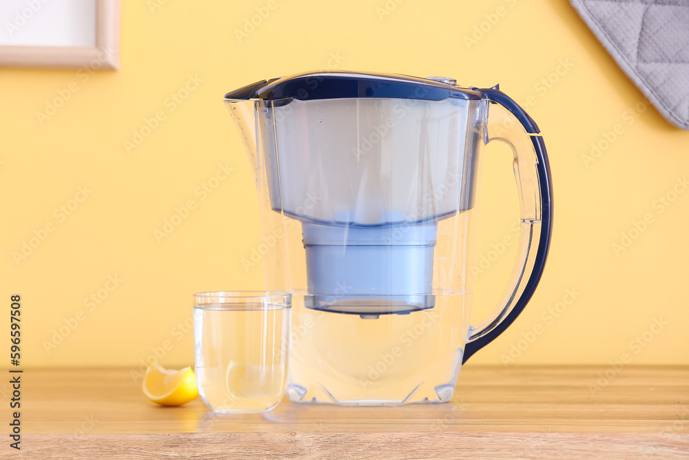 Modern filter jug, glass of water and lemon piece on kitchen counter