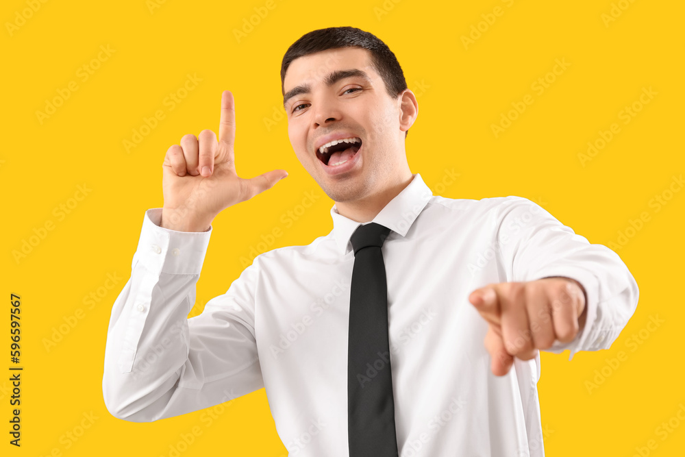 Young businessman showing loser gesture on yellow background