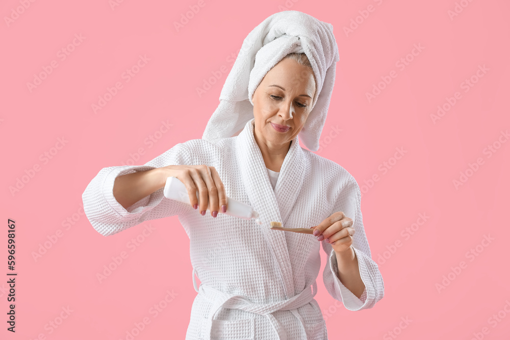 Mature woman with toothbrush and paste on pink background