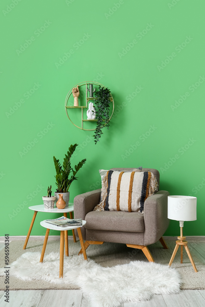 Cozy grey armchair with cushions, tables and houseplants near green wall