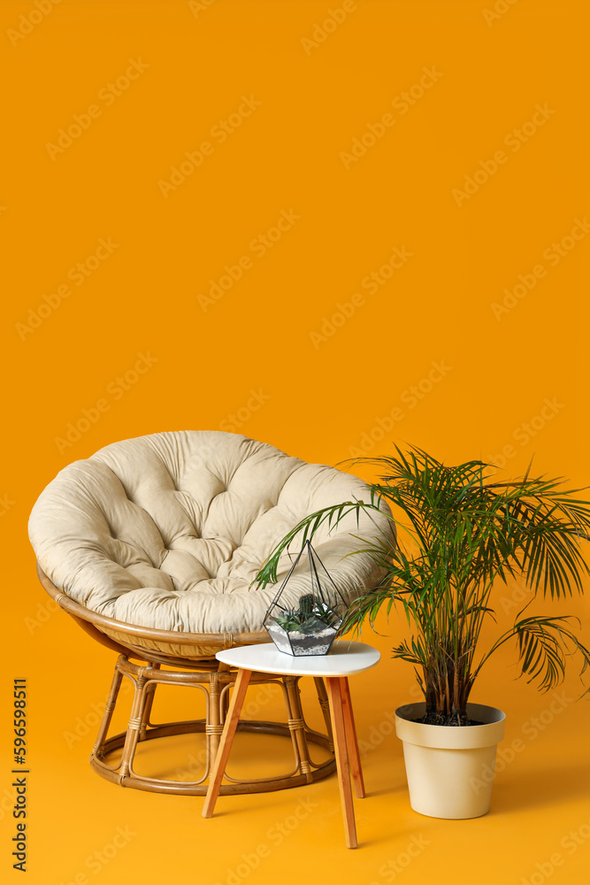 Cozy armchair, table and houseplants on orange background