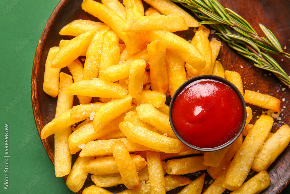 Plate with tasty french fries and ketchup on green background, closeup