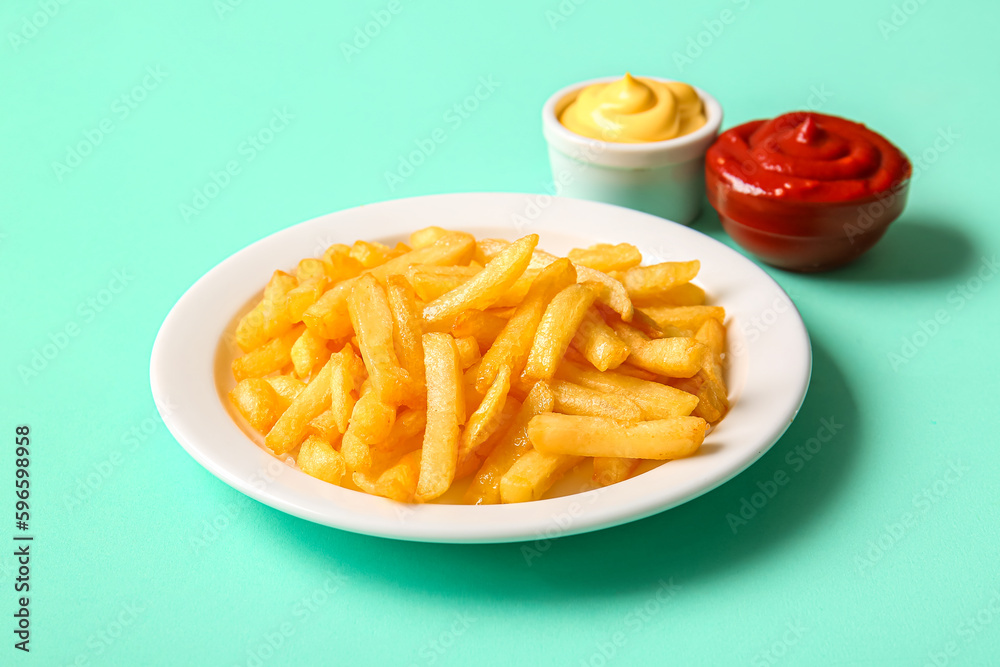 Plate of tasty french fries and sauces on color background