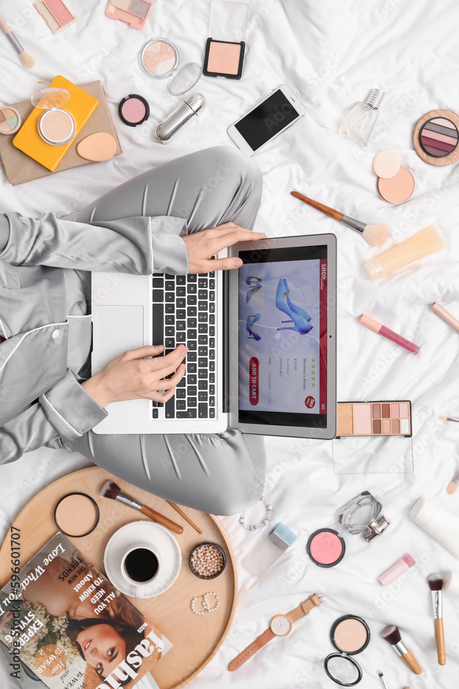 Woman with laptop, makeup products and accessories shopping online on white blanket