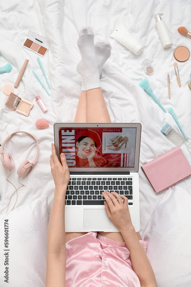 Woman with laptop, makeup products and accessories shopping online on white blanket