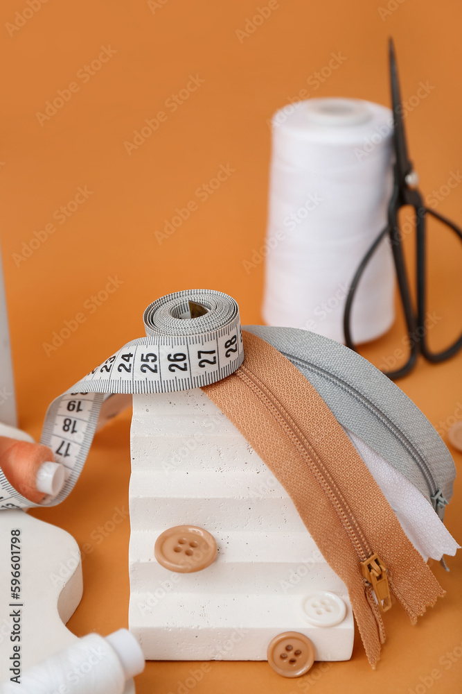 Podium with measuring tape, zips and buttons on orange background