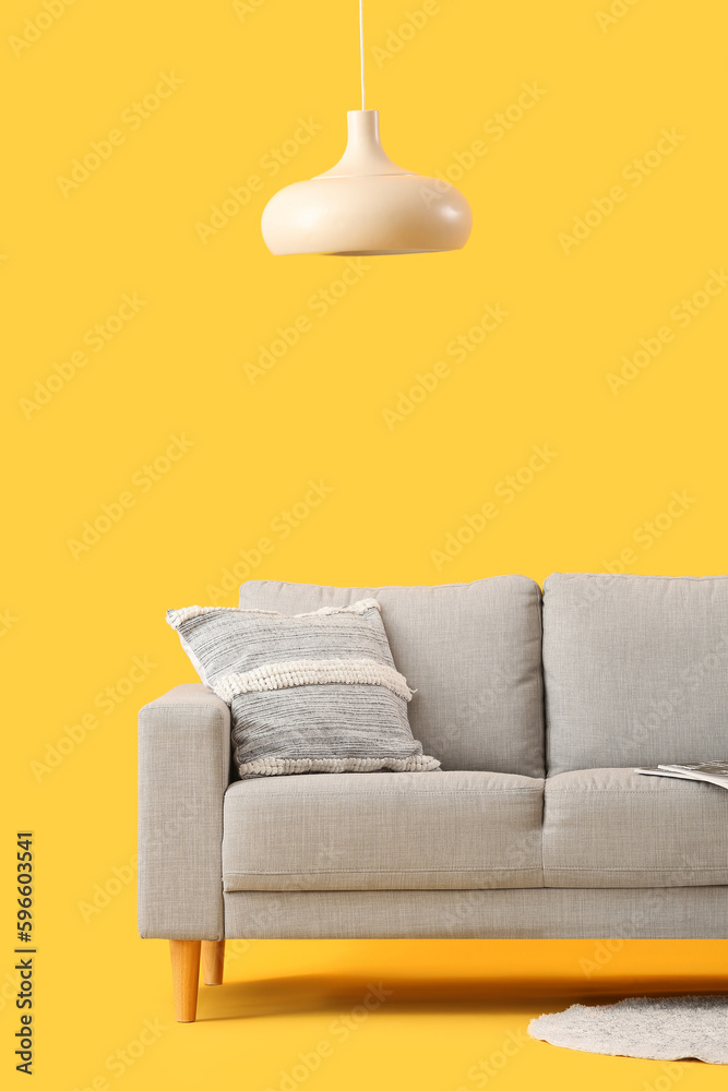 Cozy grey sofa with cushion on yellow background