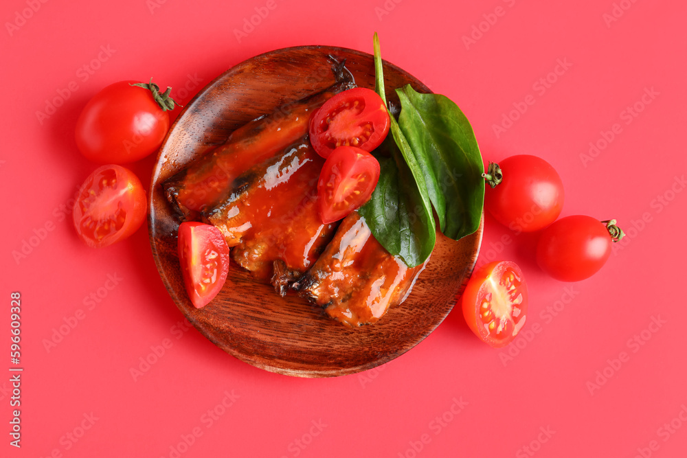 Plate with canned fish in sauce, spinach leaves and tomatoes on red background