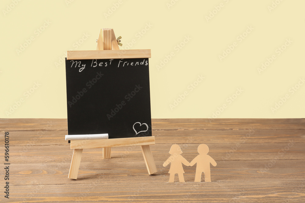 Blackboard with text MY BEST FRIEND and paper human figures on wooden table