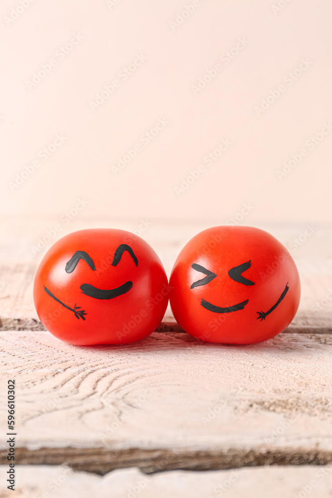 Tomatoes with happy faces on white wooden table. Friendship Day celebration