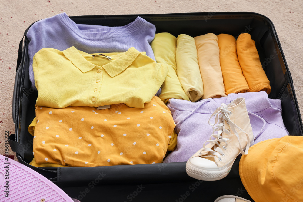 Open suitcase with clothes on beige carpet, closeup