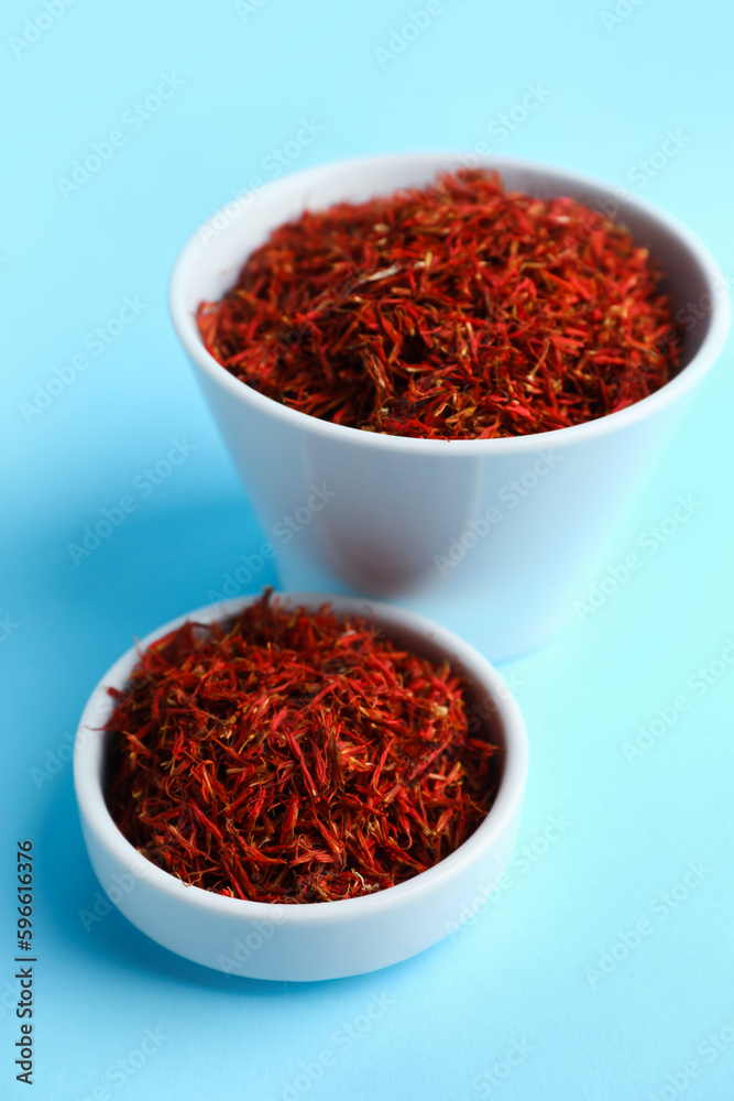 Bowls with pile of saffron on blue background