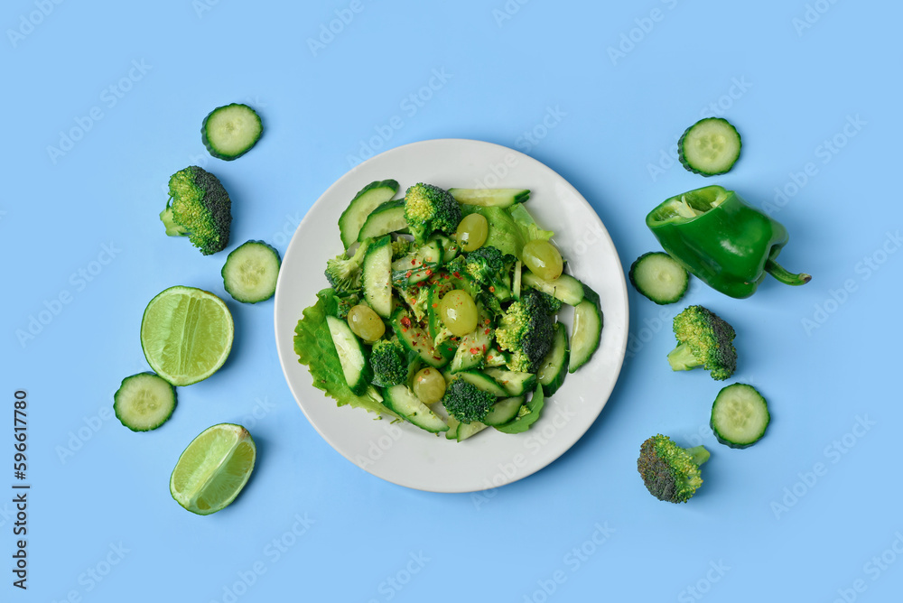 Plate with fresh salad and ingredients on blue background