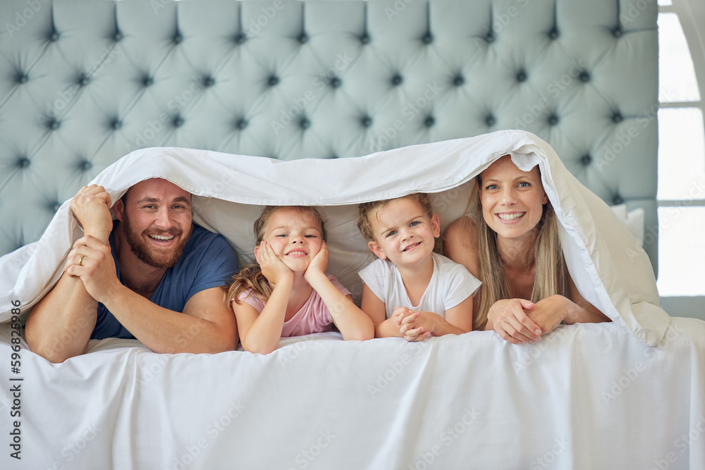 Portrait of happy parents with little children lying on bed at home under blanket. Caucasian girls b