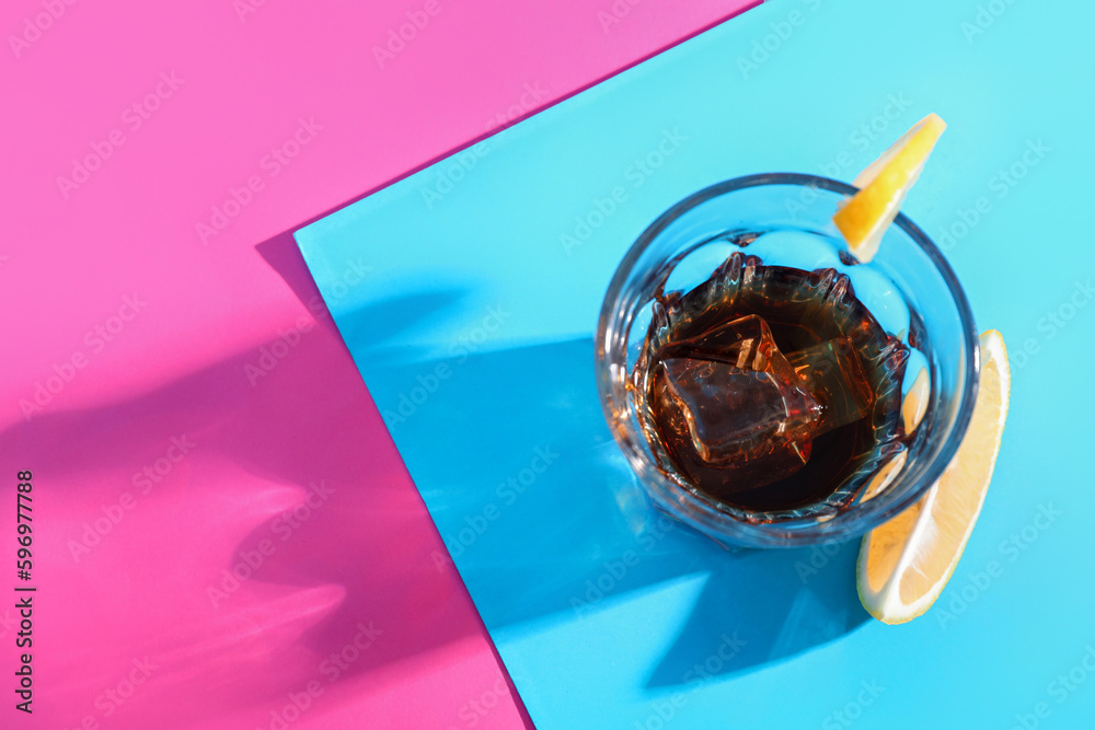 Glass of rum with lemon slices and ice cubes on colorful background