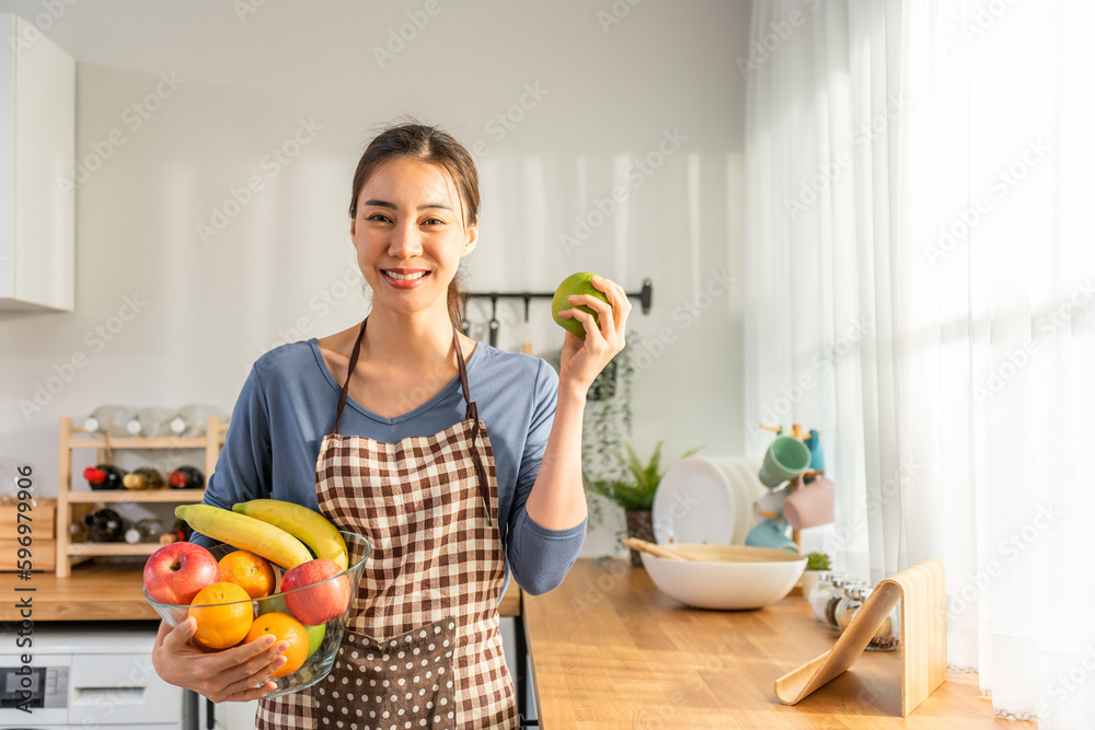 Portrait of Asian young woman hold a bowl of fruits and look at camera.