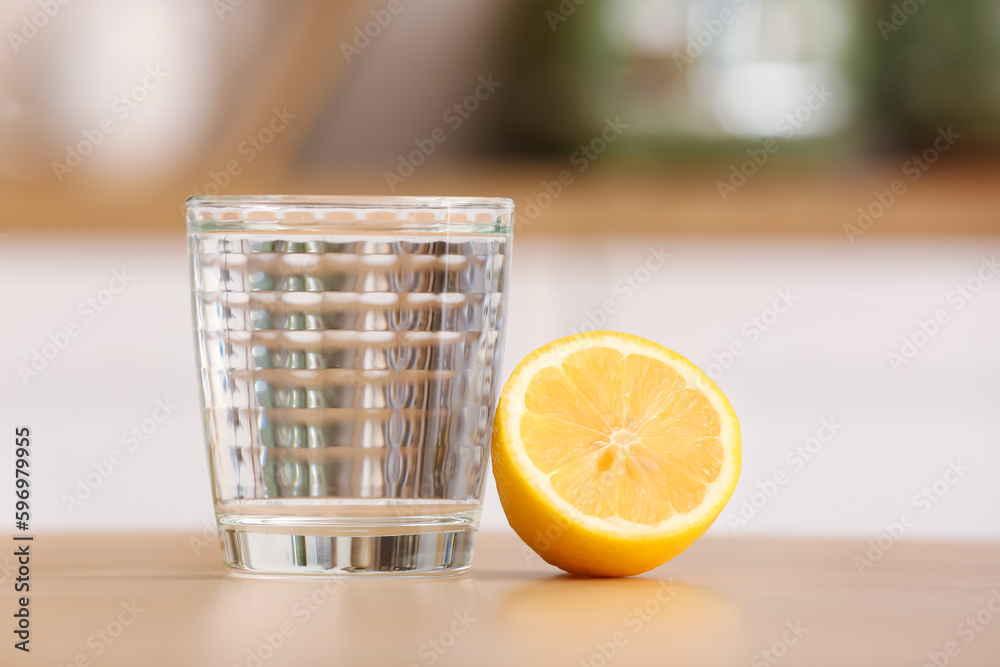 Glass of water and lemon on wooden table in kitchen