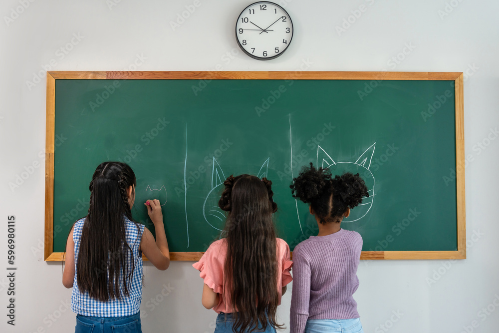 Diverse student writing blackboard in classroom at elementary school. 