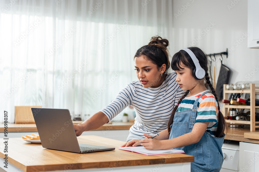 Caucasian young girl kid learning online class at home with mother. 