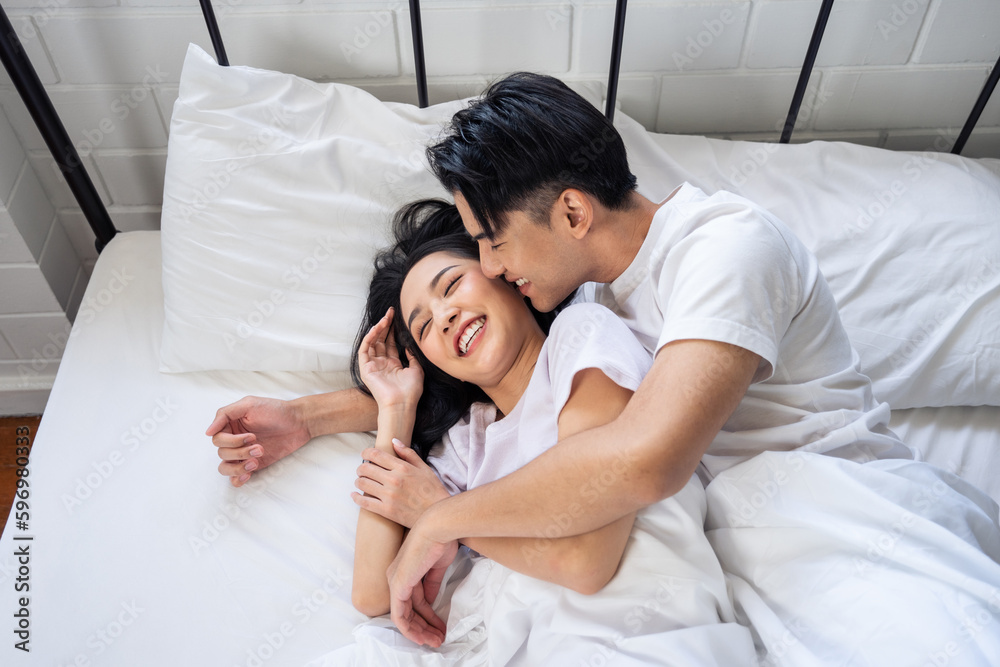 Asian husband kissing his wife while lying down sleep on bed in bedroom. 