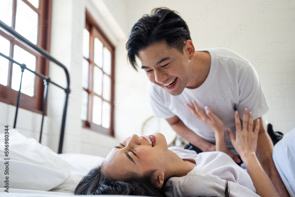 Asian attractive man tickles his girlfriend while lying down on bed. 