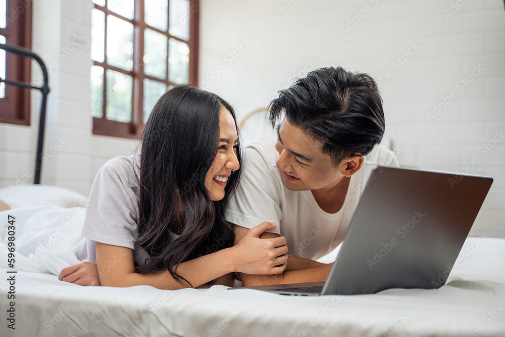 Asian attractive woman using laptop on bed with husband in the morning. 