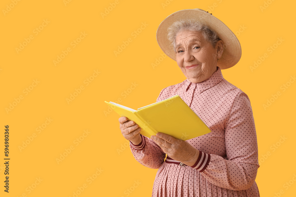 Senior woman reading book on yellow background