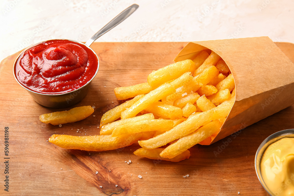 Wooden board with tasty french fries and sauces on light background, closeup