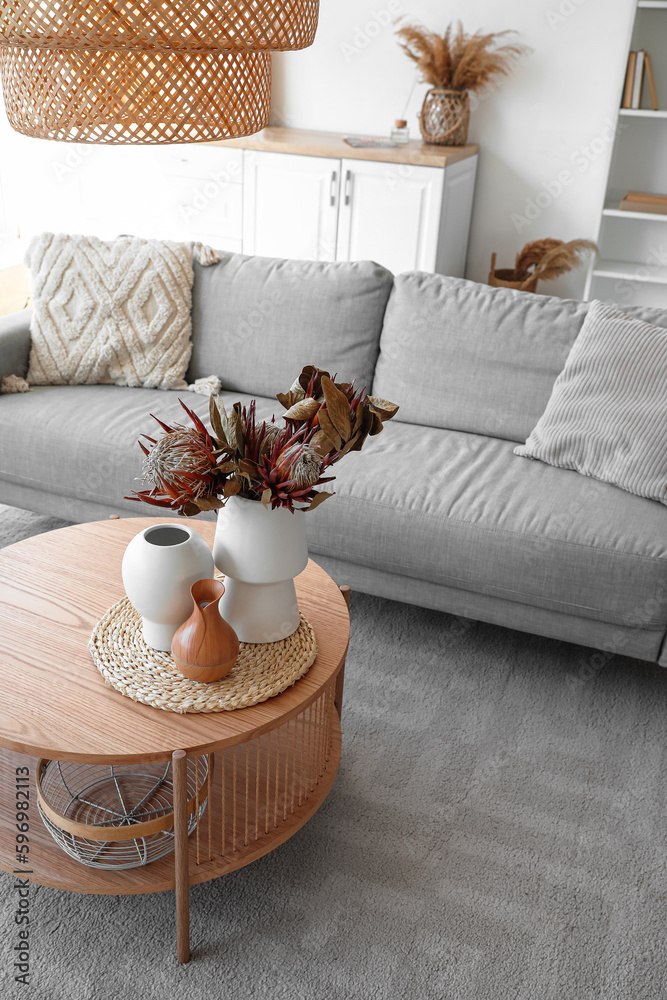 Cozy grey sofa and coffee table with bouquet of dried protea flowers in living room