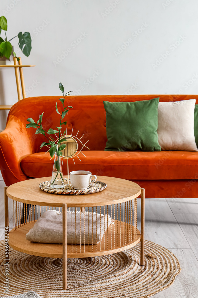 Coffee table with cup of tea, vase and mirror in interior of living room