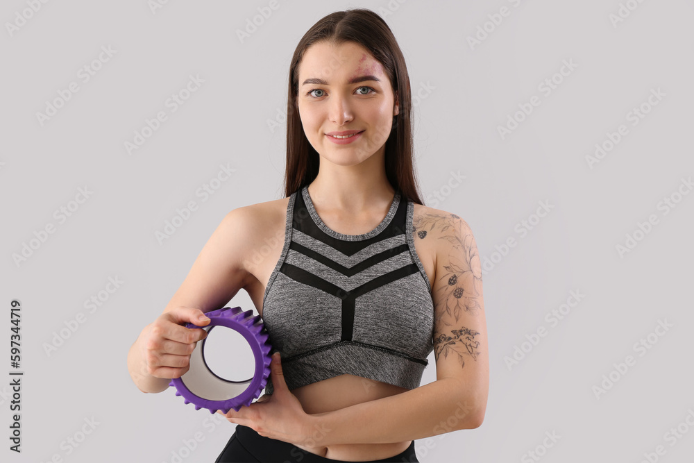 Sporty young woman with foam roller on light background