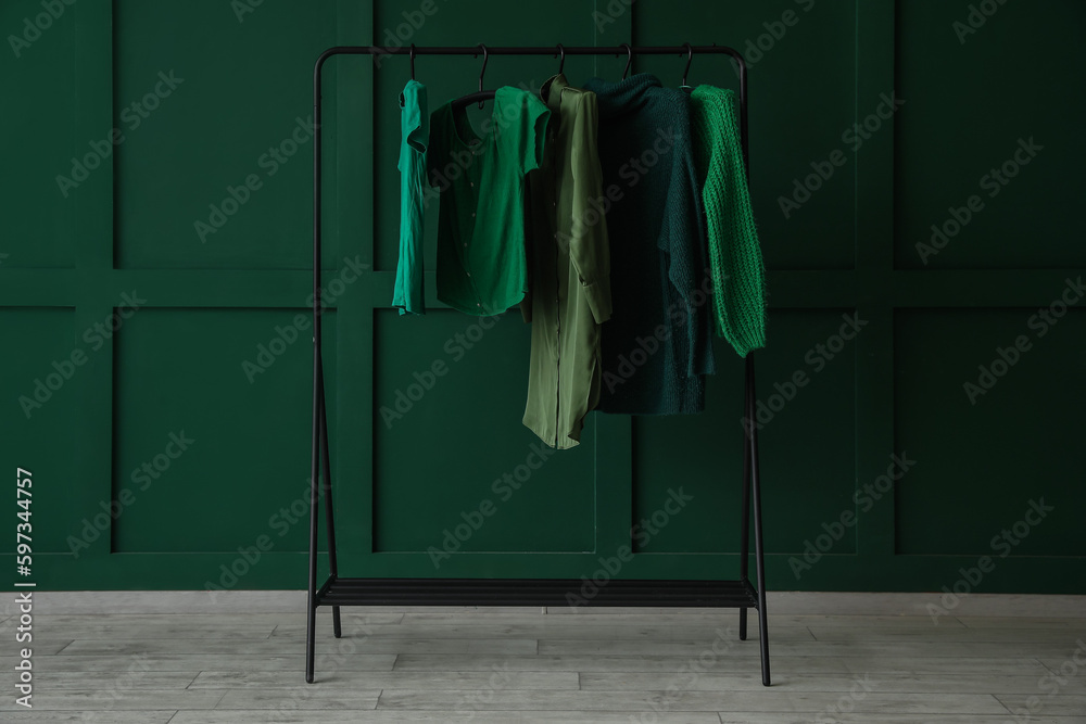 Rack with stylish female clothes near green wall