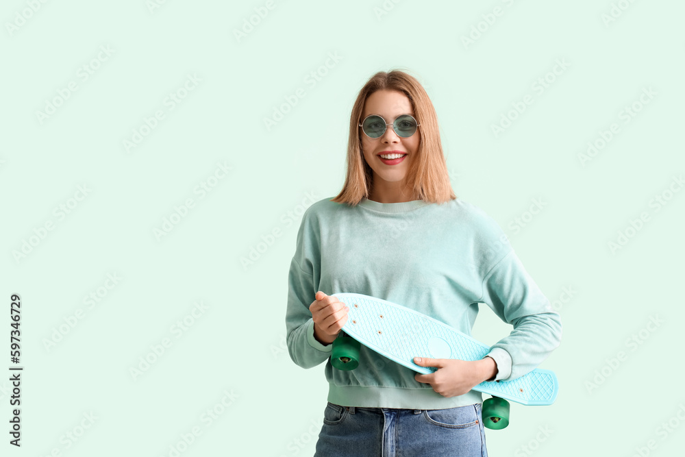 Young woman in sunglasses with skateboard on green background