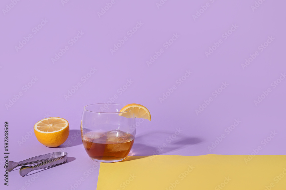 Glass of rum with ice cubes, lemon slice and tongs on colorful background