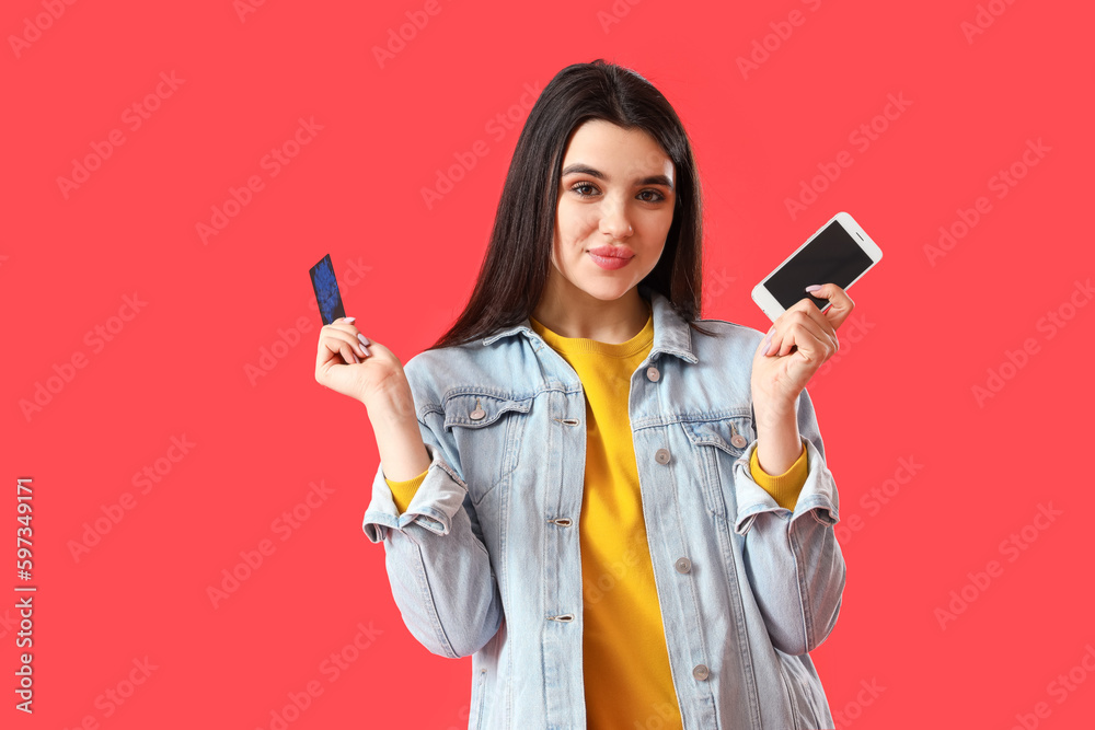 Pretty young woman with mobile phone and credit card on red background